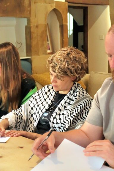 Three people seated at a table, writing notes and wearing casual clothing.