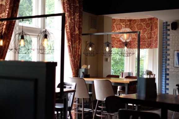 Stylish café interior with wooden tables, elegant curtains, and modern lighting.
