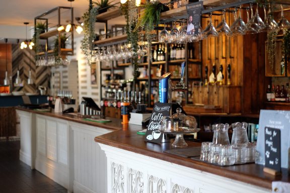 A stylish bar setting featuring wooden shelves, bottles, glasses, and a warm atmosphere.