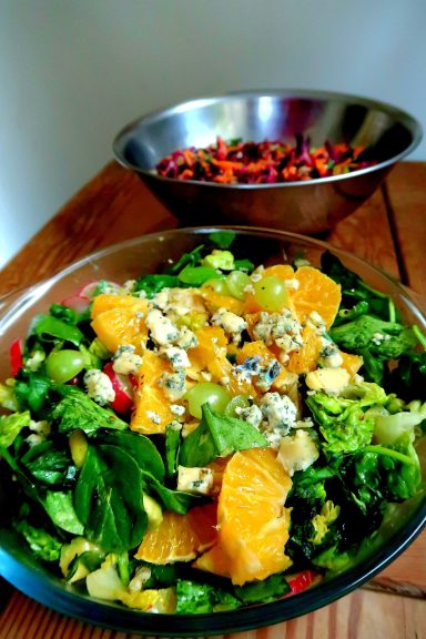 A fresh salad with greens, orange slices, and blue cheese, with a second bowl of mixed fruit.